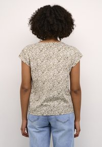 T-shirt à manches courtes dans un motif floral olive et crème dégradé. Tissu doux avec une coupe décontractée et un ourlet arrière arrondi. Associé à un jean bleu délavé.