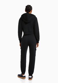 Crop hoodie nera con cappuccio, abbinata a pantaloni cargo con vita elastica e tasche laterali. Completato da sneakers nere con suola in gomma.