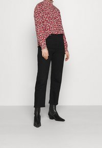 Röd och rosa blommig blus med hög hals, svarta högmidjade jeans och svarta ankelstövlar med spetsig tå och kraftig klack.