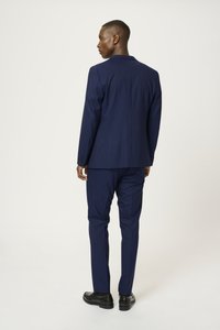 Traje azul marino con un corte ajustado, que presenta una abertura sencilla y pantalones a juego. La tela parece suave, combinada con zapatos de vestir negros.