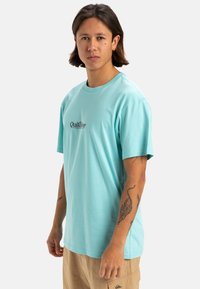 Camisa de algodón azul claro con manga corta, cuello redondo, que presenta un pequeño logo impreso en la zona del pecho.