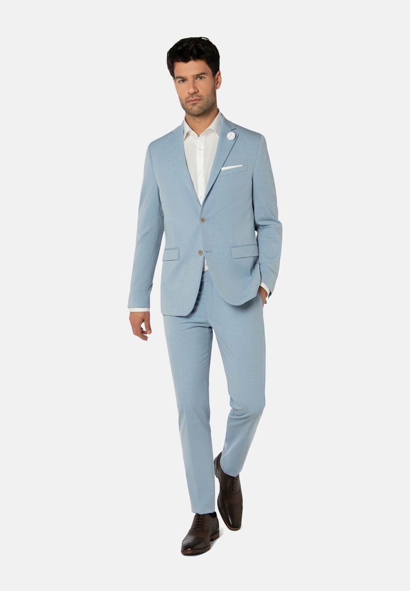 Costume bleu clair en tissu texturé, présentant une coupe ajustée, des revers crantés, une fermeture à deux boutons et des chaussures habillées marron.