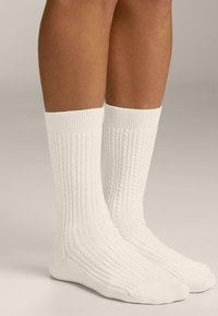 Hvide ribbede sokker lavet af bl�ødt materiale, med et tekstureret mønster og mellemhøj længde, der dækker den nederste del af læggen uden tydeligt mærke.