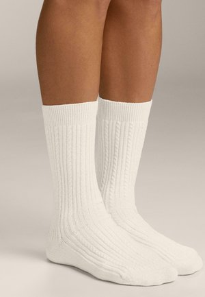 Calzini bianchi a costine realizzati in materiale morbido, con motivo testurizzato e altezza media che copre la parte bassa del polpaccio senza marchi evidenti.