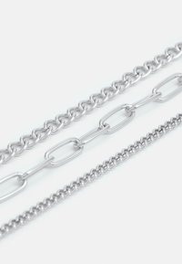 Tre sølvfargede metallkjeder: en kraftig lenke med klumpete lenker, en mellomstor lenke med avlange lenker, og en delikat kjede med små lenker.