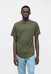 Olivově zelené tričko s krátkým rukávem, kulatým výstřihem a hladkou texturou, zkombinované se světle modrými džínami.