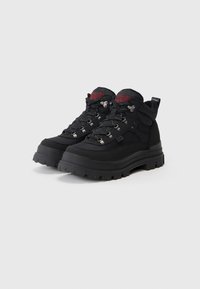 Černé turistické boty s vysokým kotníkem, syntetický svršek, silná gumová podešev, kovové doplňky a červené akcenty loga na jazyku.