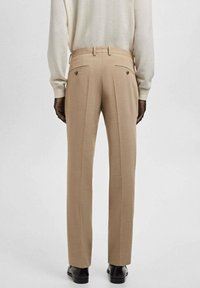 Pantalones beige con un corte entallado, que presentan dos bolsillos traseros y una textura suave. El diseño incluye detalles con pliegues de aguja y acentos cosidos.
