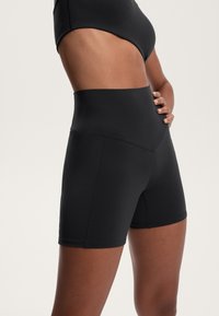 Črne kratke hlače z visokim pasom, narejene iz raztegljivega materiala, z gladko teksturo in prilegajočo zasnovo, z minimalnimi šivi in čistim zaključkom.