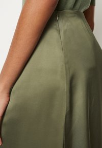 Falda de satén verde oliva con una textura suave, cinturilla ajustada y un discreto detalle de cremallera a lo largo de la costura trasera.