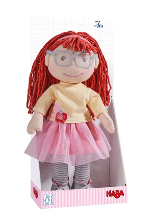 Poupée douce avec cheveux en fil rouge, lunettes grises, chemise jaune avec motif pomme, jupe en tulle rose, leggings gris rayés et chaussures grises dans une boîte.