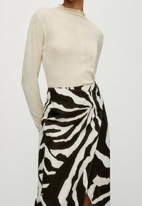 Top a maniche lunghe di colore crema realizzato in un tessuto morbido, abbinato a una gonna avvolgente a righe zebra in bianco e nero con dettaglio dei bottoni.