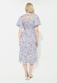 Lila Blumenkleid mit geschichteten Rüschen, durchscheinendem Stoff, kurzen Puffärmeln und einem Schlitz im Rücken. Es hat eine elegante, taillierte Silhouette.