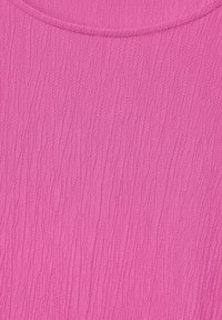 Tessuto testurizzato di un vivace colore rosa con un sottile motivo stropicciato e scollatura rotonda. Il materiale appare leggero e traspirante.