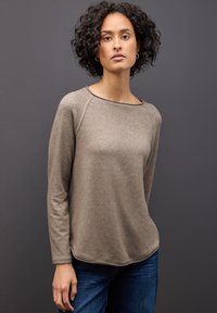 Vaaleanruskea pitkähihainen paita, jossa on pyöreä pääntie, pehmeä rakenne ja raglan-hihat, yhdistettynä farkkuihin. Yksinkertainen muotoilu, ilman kuvioita.