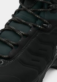Czarne buty trekkingowe z teksturową powierzchnią, zielonym materiałem i wzorzystymi sznurówkami. Zawierają plastikowe elementy oraz widoczne detale przeszycia.