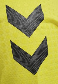 Lyst gult tekstureret stof har sorte chevron mønstre med bølgede accenter, hvilket skaber et iøjnefaldende design. Små cirkulære detaljer er til stede overalt.