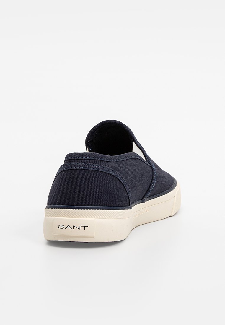Basket de couleur bleu marine à enfiler avec semelle en caoutchouc blanche, couture visible et branding "GANT" sur le talon, présentée de dos sur un fond blanc.