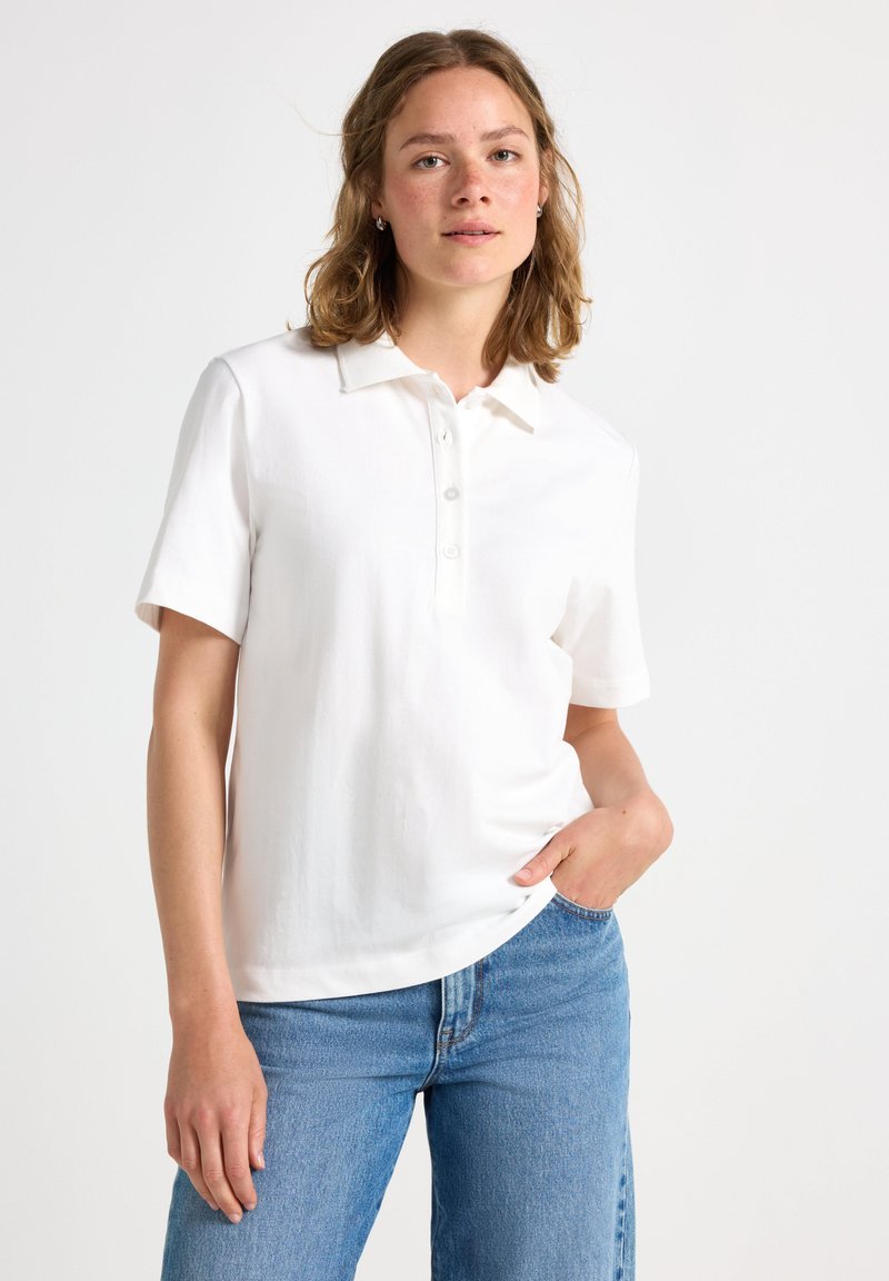 Hvid polo skjorte med korte ærmer, tre-knap lukning og en blød, glat overflade. Bæres med blå denim jeans, afslappet pasform.