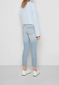 Camisa de manga larga azul claro combinada con jeans azules desgastados. Los jeans presentan detalles rasgados y un ajuste slim. Zapatillas blancas completan el atuendo.