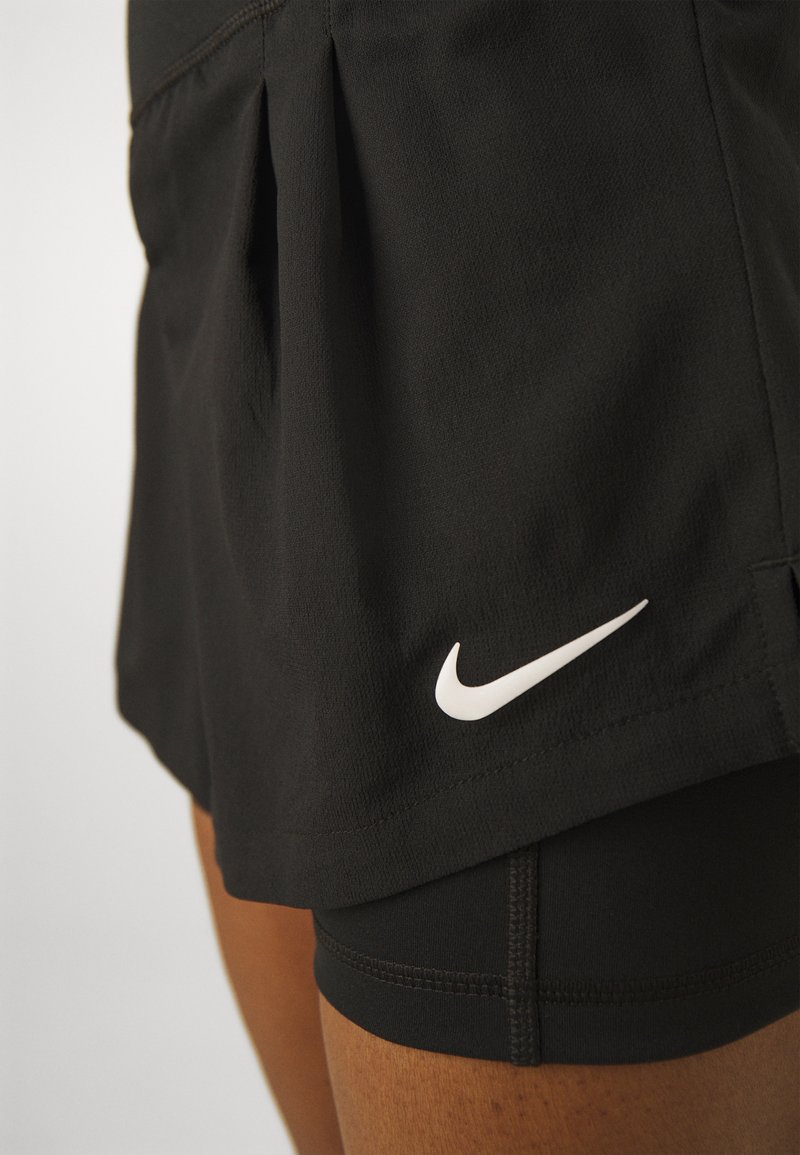 Schwarze Sportshorts mit passendem Innenfutter, das ein kleines weißes Nike-Swoosh-Logo in der Nähe des Saums am Oberschenkel einer Person zeigt.