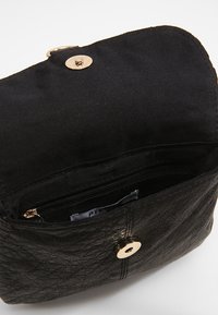 Borsa nera con esterno in pelle testurizzata, dettagli in oro e chiusura a scatto magnetica. L'interno presenta una piccola tasca con cerniera.