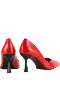 Chaussures à talons hauts en cuir rouge avec des bouts pointus et des talons aiguilles noirs. Texture lisse avec un design épuré et des côtés ouverts.