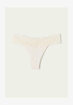 String mit Spitzenbesatz in hellem Creme mit einem weichen, glatten Stoffkörper. Der Spitzenbund hat ein florales Muster für zusätzliche Details.