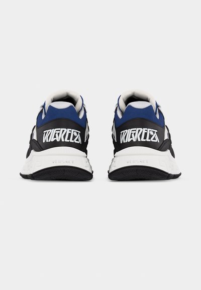 Ζευγάρι μαύρα, μπλε και λευκά αθλητικά παπούτσια, φαίνονται από πίσω, με έντονο λευκό γραφικό κείμενο στη φτέρνα και χοντρές λευκές σόλες.