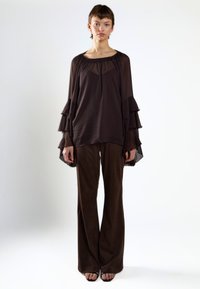 Top de chiffon marrón con mangas acampanadas combinado con pantalones de pierna ancha marrones. La tela tiene una textura suave, creando un efecto de capas.