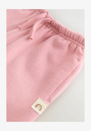 Rožinės medvilninės sportinės kelnės su elastine juosta, turinčios raištelį ir mažą etiketę su vaivorykštės dizainu ant apatinės kojos.