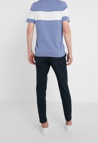 Modré tričko s krátkým rukávem, na horní části s bílým vodorovným pruhem; spárované s tmavými kalhotami a bílými botami.