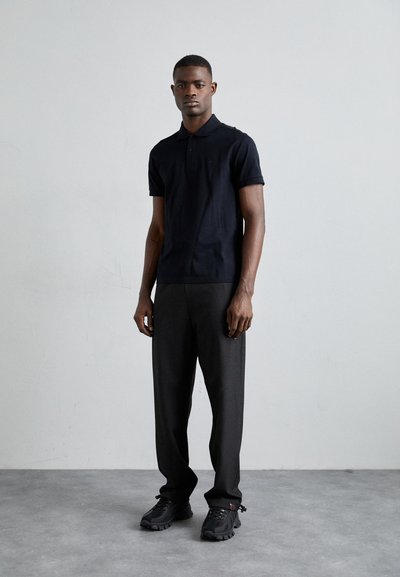 Svart polo skjorte, grå bukser og svarte sneakers; slim fit, kortermet polo, teksturert stoff og subtil merkevaremerking på skjorten.