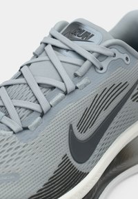 Γκρι αθλητικό παπούτσι Nike με υφασμάτινο επάνω μέρος με υφή, μαύρο λογότυπο και επίπεδες κορδόνες. Η σόλα διαθέτει λευκή μεσόσολα και σχέδιο πρόσφυσης με μοτίβο.