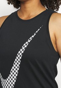 Personne portant un haut noir sans manches avec un grand logo Nike Swoosh blanc en motif pied-de-poule sur la poitrine.