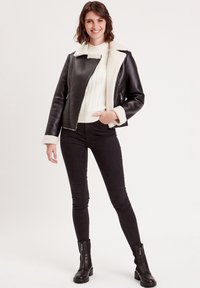 Veste en cuir noir avec col et doublure en shearling blanc, associée à un pull à mailles torsadées blanc et à un pantalon noir. Comprend des bottes zippées.