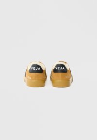 Sneakers din suede maro cu guler din blană de oaie, având un capac pe călcâi negru cu logo-ul "VEJA" și talpă din cauciuc. Partea superioară texturată.