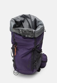 Sac à dos violet avec un bas noir et des bretelles ajustables. Comprend une fermeture à rabat grise et une étiquette d'information à l'intérieur.