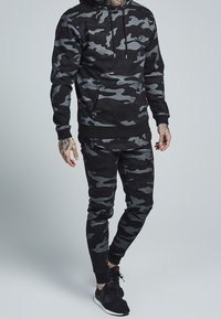 Black and gray camo-patterned hoodie and joggers, made from a textured fabric. Features a drawstring hood and fitted cuffs.