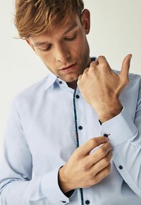 Hele sinine tekstuurne särk nööpidega kaelusega. Omab kontrastset mustriga sisekrae ja tumedaid nuppe varrukatel ja ees.