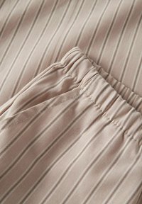 Tissu beige clair avec de fines rayures verticales, doté d'une taille élastique et de détails de poches cousues pour le confort et l'ajustement.