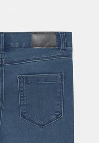 Dark blue denim jeans with a leather patch at the waistband, a single back pocket, and visible stitching details on the fabric.