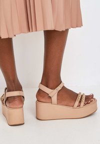 Beige platform sandalen met een chunky heel, een ontwerp met meerdere banden en gouden kettingaccenten. Gladde leren textuur met een verstelbare enkelband.
