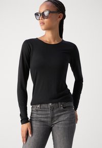 Musta pitkähihaisen paita, jossa on pyöreä pääntie, valmistettu sileästä kankaasta, yhdistettynä harmaisiin slim fit -farkkuihin. Aurinkolasit täydentävät ilmeen.