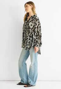 Black and white patterned blouse with long sleeves, collar, and side slits, paired with light blue wide-leg jeans and black sandals.