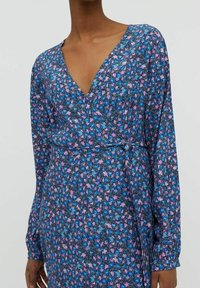 Robe portefeuille à motifs floraux avec un décolleté en V, des manches longues et une base bleue ornée de fleurs roses et violettes. Tissu doux avec une taille nouée.