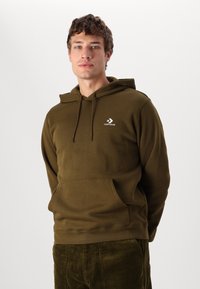 Sudadera verde oliva con un bolsillo frontal, capucha con cordón y logo blanco de Converse en el pecho izquierdo. Tela suave, corte relajado.