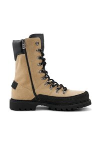 Béžová semišová bota s černým koženým vrškem, bočním zipem a černým šněrováním. Má texturovanou černou gumovou podrážku s hlubokým vzorkem.