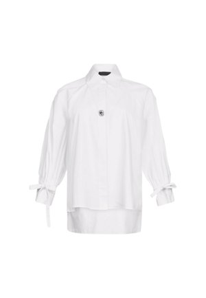 Camicia bianca, maniche lunghe a sbuffo con dettaglio a fiocco, chiusura con bottoni al colletto, vestibilità comoda, tessuto liscio e leggermente lucido.