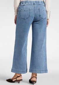 Jeans larges bleu clair avec une taille élastique. Comprend deux poches arrière et un ourlet retroussé. Texture de denim lisse.